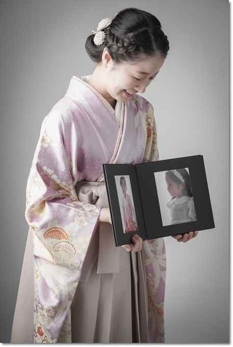 子供の頃のアルバムを持って卒業式の記念写真 薄紫色の振袖にベージュの袴